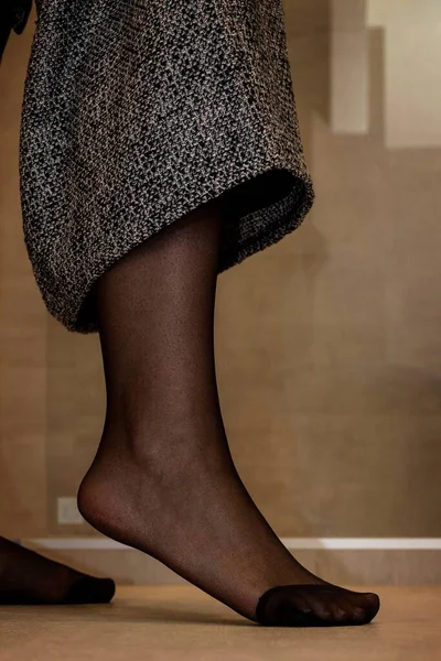 A close up portrait of a foot in sexy black pantyhose of a girl pulling up her skirt. The nylon is reinforced at the toes.