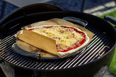 Pizza taşının üzerine uzanmış bir pizza margherita portresi ve mangal ızgarasında bir parça fırın kağıdı. Lezzetli pizzanın üzerinde peynir ve domates sosu var..