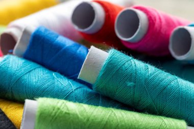 Birbirinin üstünde duran birden fazla iplik makarasının portresi. Her rulo lifin farklı bir rengi var. İplik ya da tel bazı dikiş projelerinde kullanılmak üzere hazır..