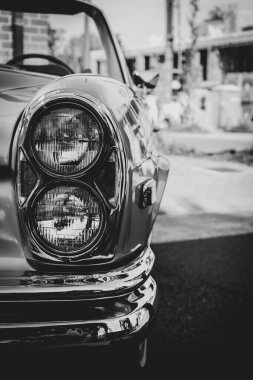 Arka taraftaki eski bir arabanın ön sağ farının siyah beyaz portresi. Direksiyon görünür ama bulanıktır..