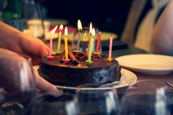 木製のお祝いのテーブルの上にろうそくを燃やしてチョコレートの誕生日ケーキを置く人の肖像画 爆破される準備ができて食事とお祝いを始めます — ストック写真
