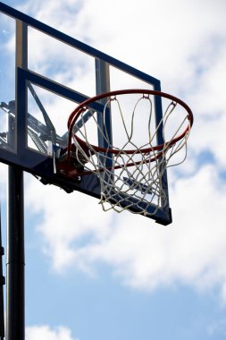 Mavi bir gökyüzünün önünde üzerinde mavi çizgiler olan, üzerinde ağ ve pleksiglas sehpası olan ayarlanabilir bir basketbol çemberi portresi. Basketbol potası ya da halka turuncu ve direği siyah..