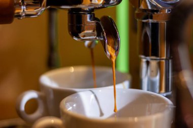 Bir kahve makinesinin hortumunun portresi. Hortumdan yeni çıkmış taze topraklanmış sıcak kahve var. İki beyaz fincanda..