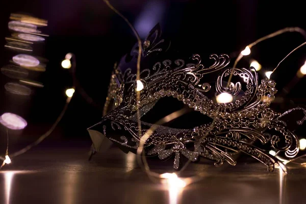 A portrait of a venetian mask full of mystery on a wooden table surrounded by lights. It is perfect to hide someones identity on a masked ball.