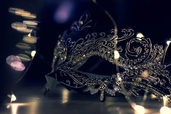 A portrait of a venetian mask in the mysterious evening light on a wooden table surrounded by lights. It is perfect to hide someones identity on a masked ball.