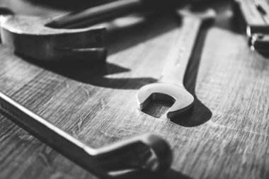 Siyah beyaz bir çekiç portresi, açık uçlu ve tahta bir masanın üzerinde duran bir İngiliz anahtarı. Aletler bir inşaat işi ya da bir çeşit tamir işi için kullanılıyor..