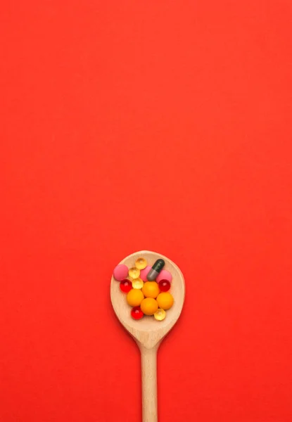 Píldoras Multicolores Una Cuchara Madera Sobre Fondo Rojo Concepto —  Fotos de Stock