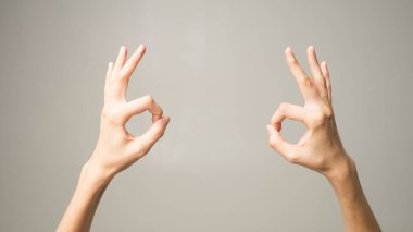 Genç bayan mutlu görünüyor, gülümsüyor, el kol hareketi yapıyor, tamam işareti gösteriyor. Beyaz kadın parmaklarıyla iyi niyet gösterisi yapıyor. Vücut dili kavramı