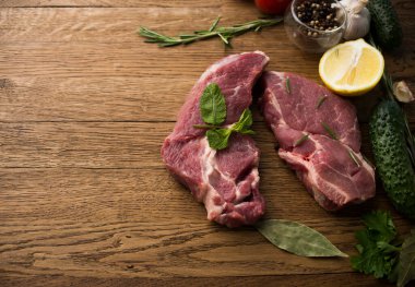 Çiğ sulu biftekler ahşap bir arka planda kızartılmaya hazır.