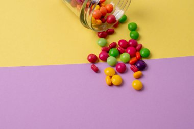 Renkli bir arka planda cam bir kavanozdan renkli şekerler döküldü.