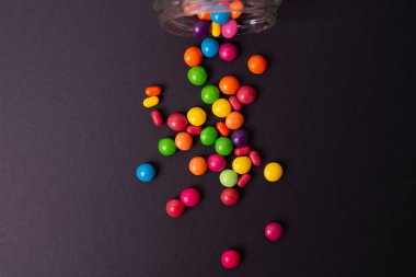 Renkli bir arka planda cam bir kavanozdan renkli şekerler döküldü.