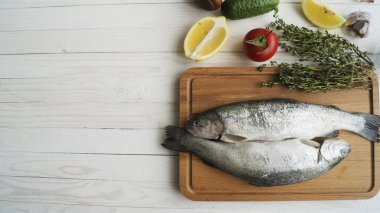 İki gökkuşağı alabalığı bir tahtada, otlarla birlikte, pişirmeye hazır..