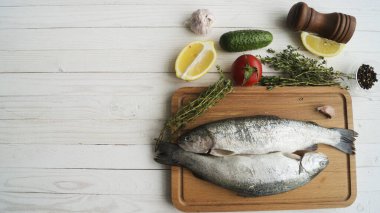 İki gökkuşağı alabalığı bir tahtada, otlarla birlikte, pişirmeye hazır..