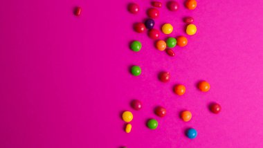 Renkli bir arka planda cam bir kavanozdan renkli şekerler döküldü.