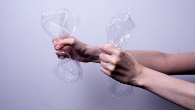 Gri arka planda şeffaf plastik ambalaj tutan kadın eli