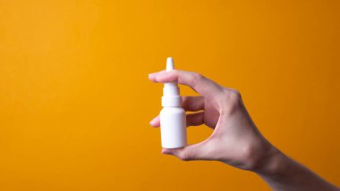 Sarı arka planda bir şişe burun damlası. Buruna sprey sık. Yukarıdan görüntüle