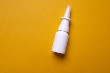 Sarı arka planda bir şişe burun damlası. Buruna sprey sık. Yukarıdan görüntüle