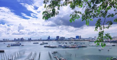 Gökyüzü bulutlarla dolu, şehrin yeşil dalları ve denizde bir teknesi var..