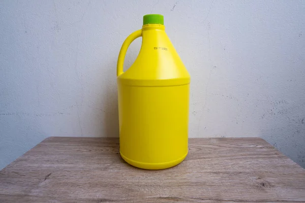 The yellow gallon has a single green lid placed alone and can be used to hold various liquids.