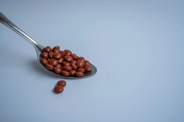 Kırmızı multivitamin hapları, beyaz arka planda kaşıkla kepçelenmiş..
