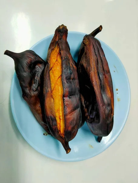 Grilled bananas, placed in a plastic plate, peeled ajar until the meat inside, looks delicious