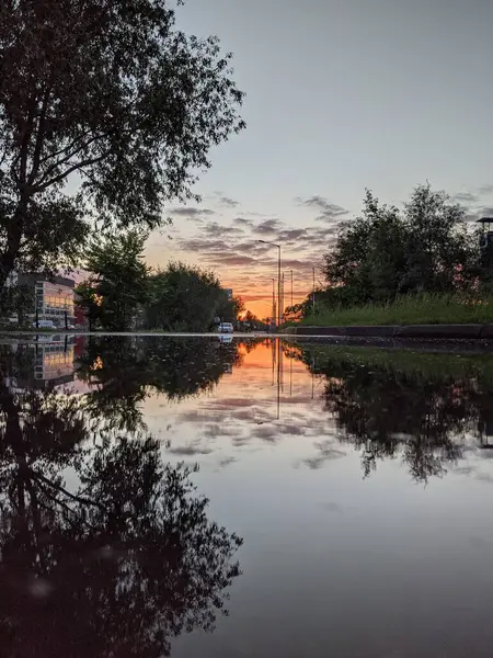 Kırmızı günbatımı, ağaçlar ve bulutlar suda yansıyor.