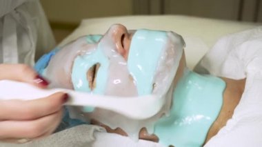 Bir kozmetikçi, deriyi beslemek için hastanın boynuna mavi bir maske takar.. 