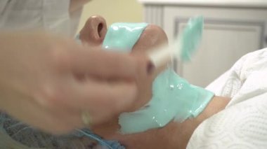 Bir kozmetikçi hastanın boynuna cildini beslemek, nemlendirmek ve tazelemek için bir ürün koyar. Klinikte estetik ameliyat. Hastanın yüzüne yakın çekim.