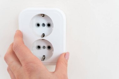 Kadın eli elektrikli bir soket tutuyor. Duvara yeni soket takıyorum. Prizleri elektrik kablolarına bağlar