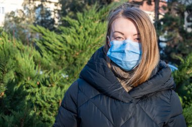 Sarışın kız kamera karşısında yüz maskesi takıyor.