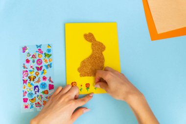 Paskalya dekoru. Renkli kağıttan yapılmış renkli bir el yapımı. Makas, karton, tavşan, tavşan. Mavi arka planda sanat yaratıcılığı. Üst görünüm, boşluğu kopyala. Basamaklardaki talimatlar.