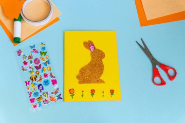 Paskalya kartları kağıttan. Mavi arka planda tavşanlı cildi selamlama kartları. Üç boyutlu. Hediye fikri, dekor ilkbaharı, Paskalya. Adım adım. Üst Manzara. Süreç çocuk zanaatı.