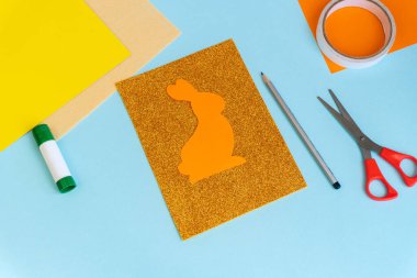 Paskalya kartları kağıttan. Mavi arka planda tavşanlı cildi selamlama kartları. Üç boyutlu. Hediye fikri, dekor ilkbaharı, Paskalya. Adım adım. Üst Manzara. Süreç çocuk zanaatı.