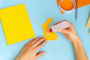 Paskalya tavşanı, çocuklar için kolay zanaatlar, renkli kâğıttan tebrik kartlarıyla bembeyaz yatıyordu. Adım adım. Bahar, Paskalya. Konsept: Paskalya için çocuk el işi. Basamaklardaki talimatlar.