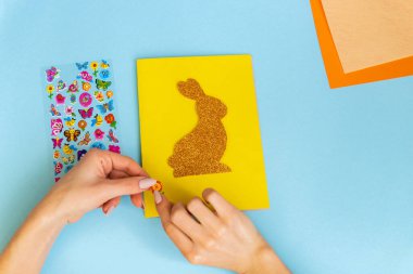 Paskalya dekoru. Renkli kağıttan yapılmış renkli bir el yapımı. Makas, karton, tavşan, tavşan. Mavi arka planda sanat yaratıcılığı. Üst görünüm, boşluğu kopyala. Basamaklardaki talimatlar.