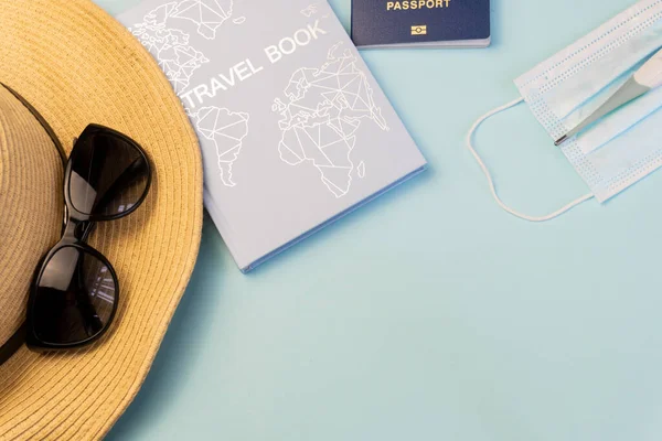 Safe travel during coronavirus pandemic concept,  vacation during the coronavirus pandemic, Covid-19. Hat, glasses, travel book, biometric passport, mask, thermometer on a blue background,  flatlay, copy space for text