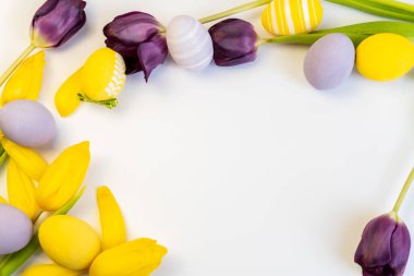 Paschal tebrik kartı. Beyaz arka planda renkli yumurtaları ve laleleri olan neşeli paskalya çerçevesi. Bahar çiçekleriyle şablon, dekorasyon tasarımı.