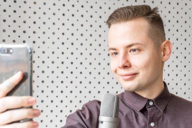 Blogcu adam video bloğunu evde kaydediyor. Adam video blogunu kaydediyor. Genç adam blog kanalı için bir video kameranın önünde konuşuyor. Vlog kaydedicisi akıllı telefon kullanarak çevrimiçi yayın yapıyor, seçici odak