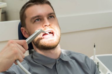 Ağız boşluğunu önlemek için dişçi muayenehanesini ziyaret eden sakallı yakışıklı bir genç. Dişçiye gitmek, doğum kontrolü. Diş hekimliği, diş bakımı ve onay kavramı.