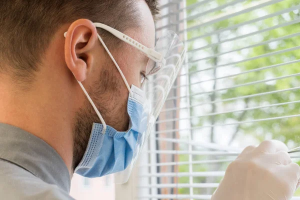 Portrait of male doctor nurse scientist medical worker wears goggles and respirator,looking out the window with sad gaze,fear and anxiety in eyes, fighting covid-19 pandemic