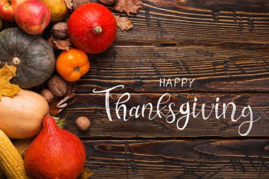 Şükran Günü selamları. Balkabakları, sebzeler, fındıklar, ahşap arka planda kuru yapraklar, üst manzara. Kaligrafik büyük harf yazımı.