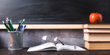 Concept to teacher's day. Pens, apple, pencils, books and glasses on the table, against the background of chalkboard. Back to school, copy space.