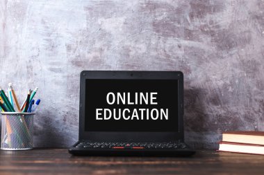 Inscription on leptop screen, online education. The concept of distance learning. Pens, pencils, books and glasses on table.