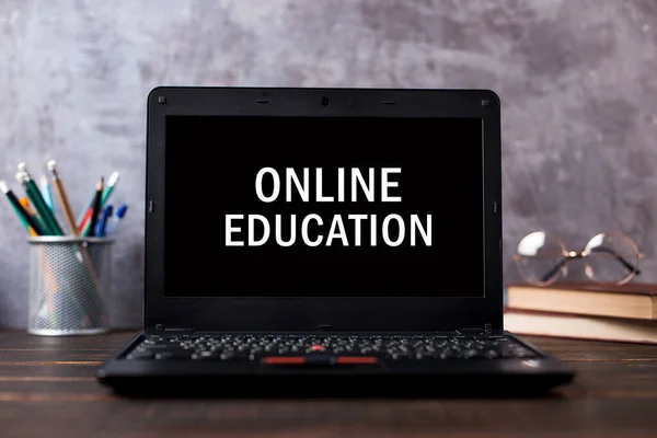 Inscription on leptop screen, online education. The concept of distance learning. Pens, pencils, books and glasses on table.