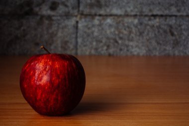 Kırmızı elma dramatik aydınlatma, ahşap bir masa üzerinde seçici odak.