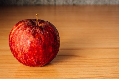 Kırmızı elma dramatik aydınlatma, ahşap bir masa üzerinde seçici odak.