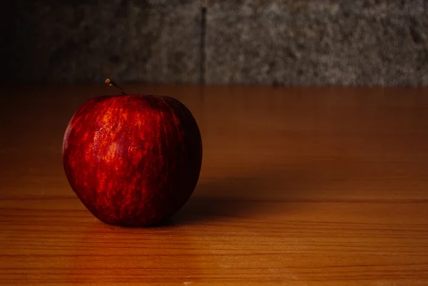 Kırmızı elma dramatik aydınlatma, ahşap bir masa üzerinde seçici odak.