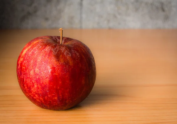 Kırmızı elma dramatik aydınlatma, ahşap bir masa üzerinde seçici odak.