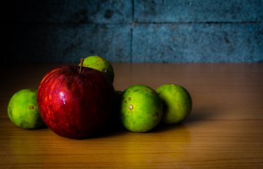 Kırmızı elma ve limon dramatik aydınlatma, ahşap bir masa üzerinde seçici odak.