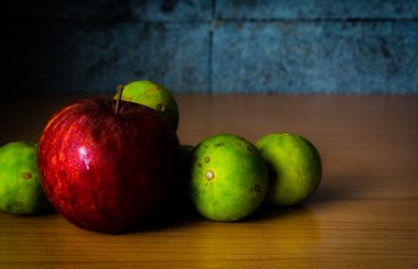 Kırmızı elma ve limon dramatik aydınlatma, ahşap bir masa üzerinde seçici odak.